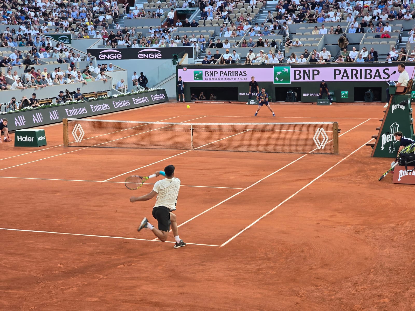 Carlos Alcaraz golpea una bola en la pista central de tierra batida de Roland Garros, con la grada al fondo.