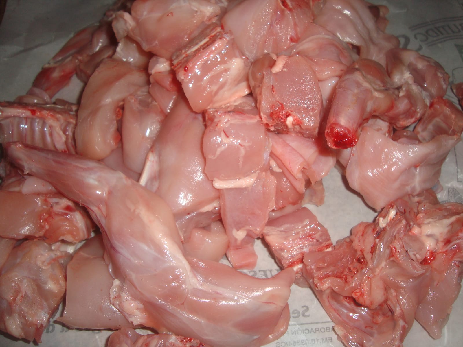 Montón de piezas de conejo crudo troceado, con patas, lomos y costillar, sobre papel de carnicería.