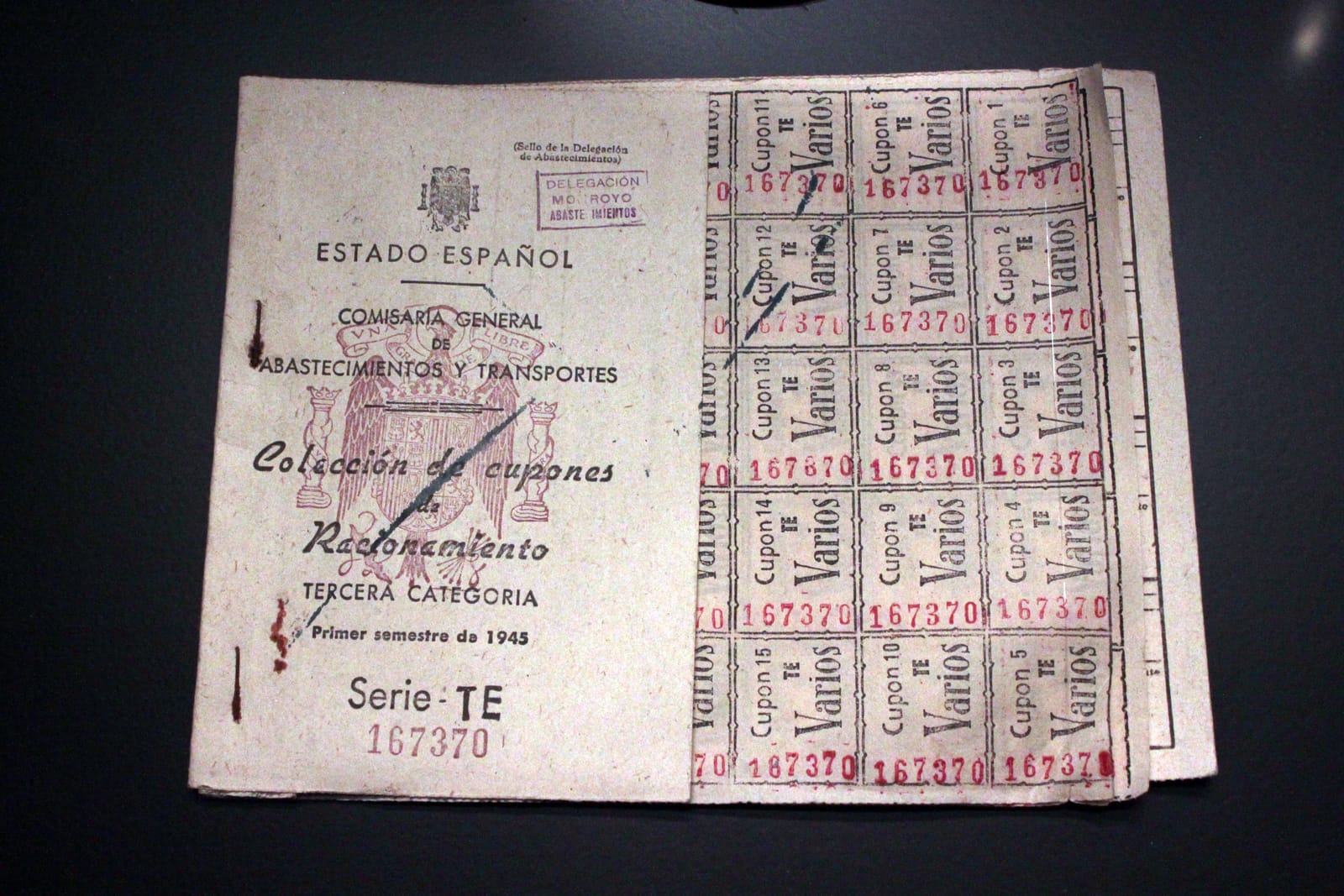 Cartilla de racionamiento española del primer semestre de 1945, de tercera categoría, abierta sobre una superficie oscura, con su portada del Estado Español y una hoja de cupones numerados.