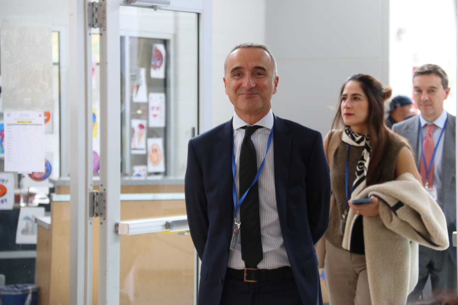 Pere Joan Pons, un hombre de pelo corto y canoso, sonriente, con traje azul marino, corbata negra y acreditación azul al cuello, entra en un edificio seguido de dos personas con acreditaciones.