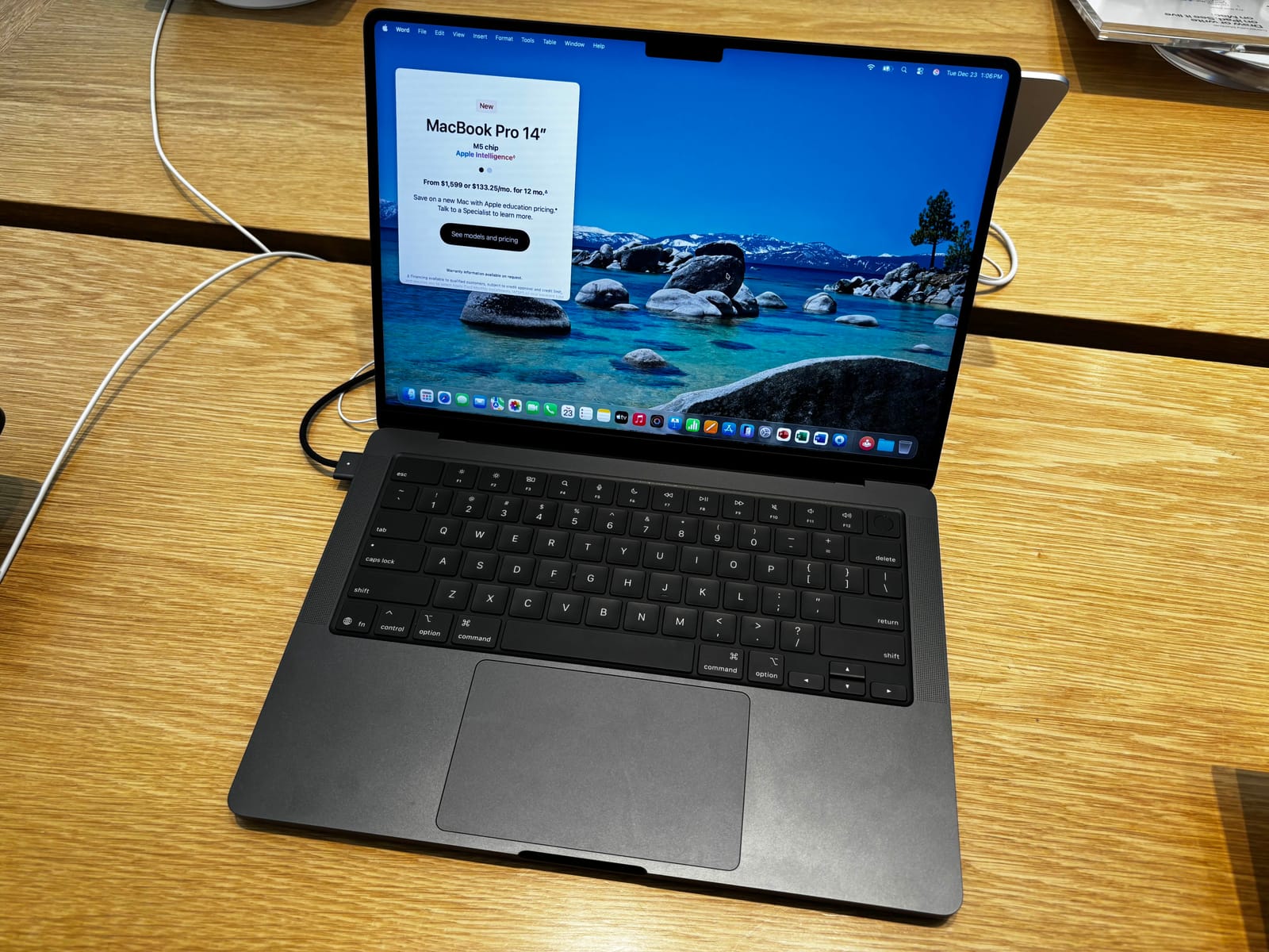MacBook Pro de 14 pulgadas en color negro espacial, abierto sobre una mesa de madera clara, con el escritorio de macOS en pantalla y la muesca de la cámara en el borde superior.