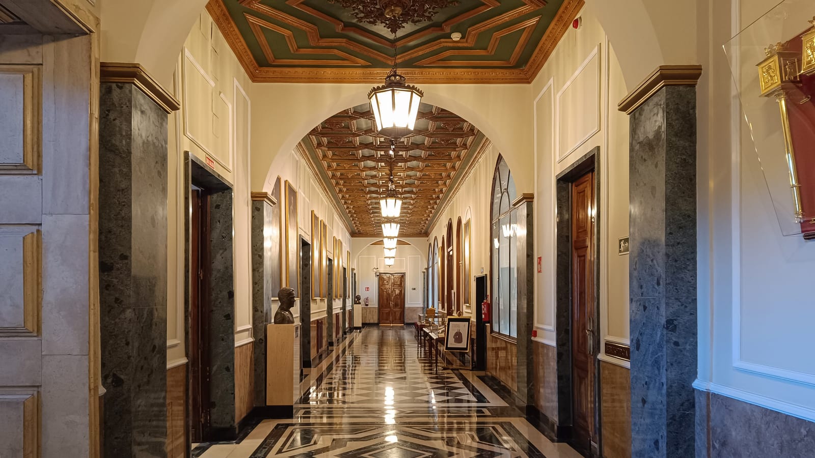 Galería interior del Palacio del Senado en Madrid, con suelo de mármol, lámparas y techos decorados.